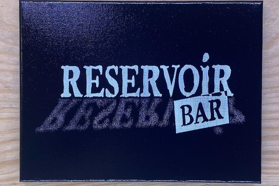 Black and white logo of Reservoir Bar on a wood surface with mirrored text effect.