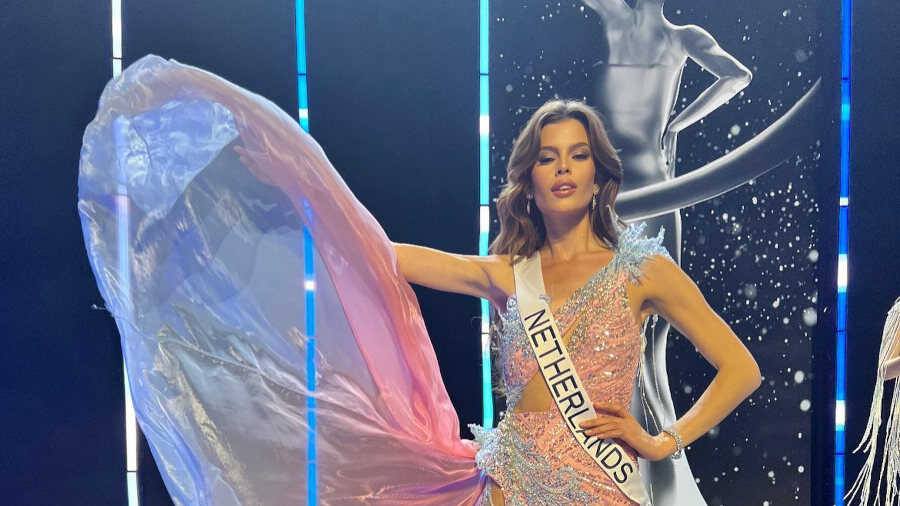 Rikkie Kollé en robe rose-bleu-blanc posant fièrement sur scène à Miss Universe 2023 au Salvador.