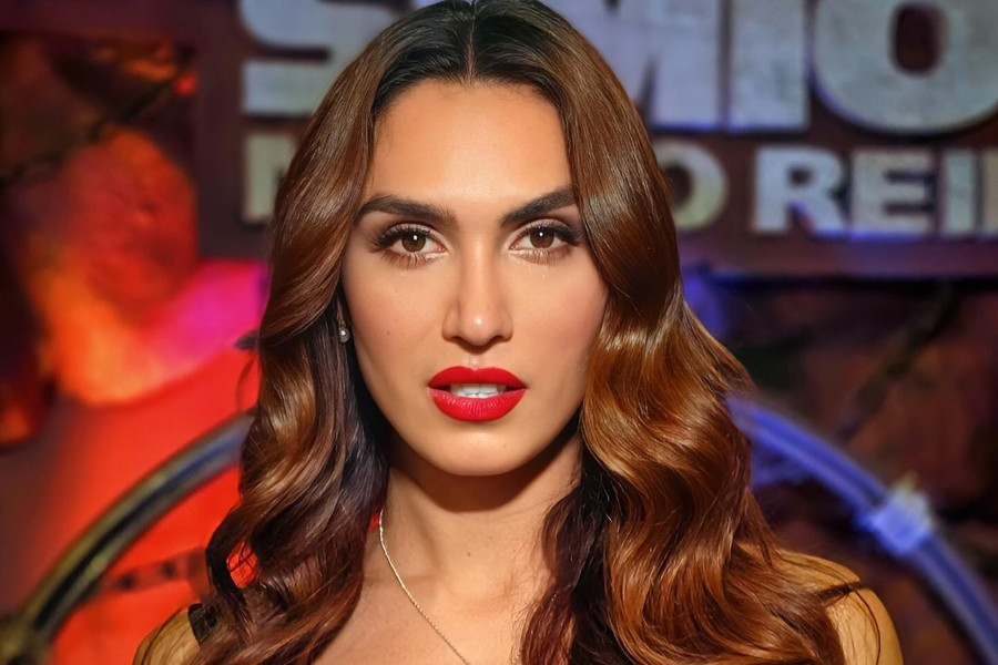 Primer plano de Isabella Santiago posando en el set de LCDLFC, con lápiz labial rojo y un colgante en forma de corazón.