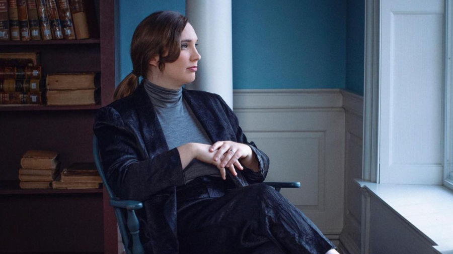 Sarah McBride sentada junto a una ventana en el Old State House de Dover, Delaware, con un traje de terciopelo oscuro y mirada contemplativa.