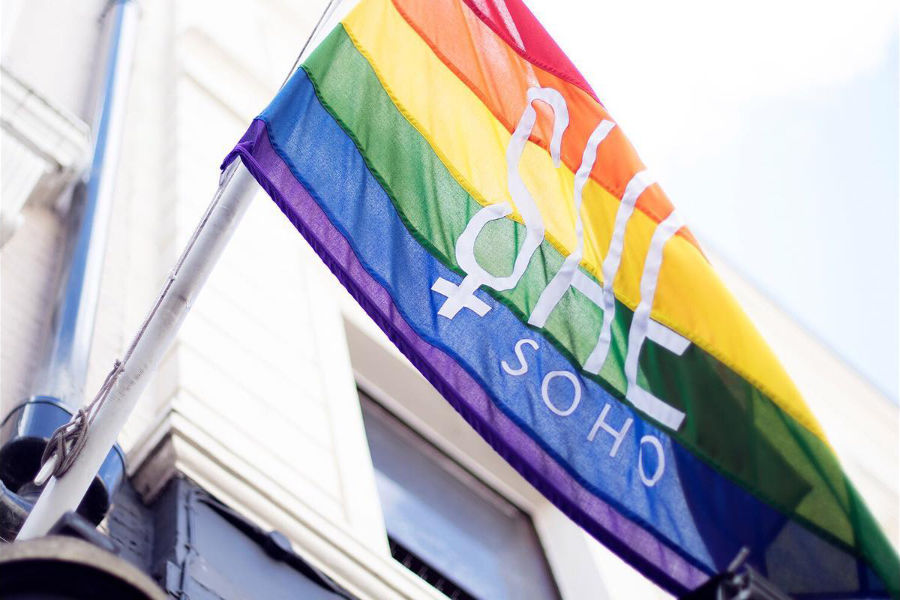 Rainbow LGBTQ+ flag with “She Soho” logo flying on building wall during Pride weekend in London.