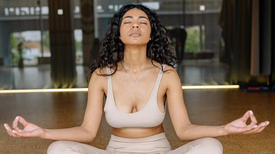 Serene woman in beige sportswear meditates on a wooden floor with closed eyes, focusing on calm breathing and inner peace.