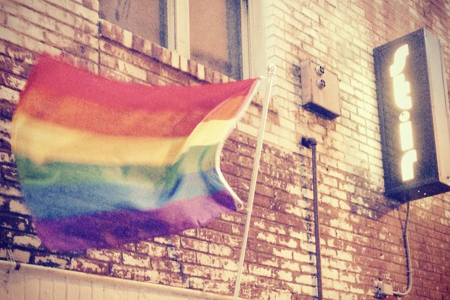 Rainbow Pride flag waving beside the illuminated Stir Lounge sign on a brick wall in Philadelphia.