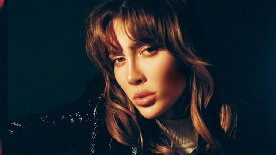 Teddy Quinlivan dans un portrait en lumière tamisée, portant une veste style varsity noire et blanche, cheveux en bataille et regard intense.