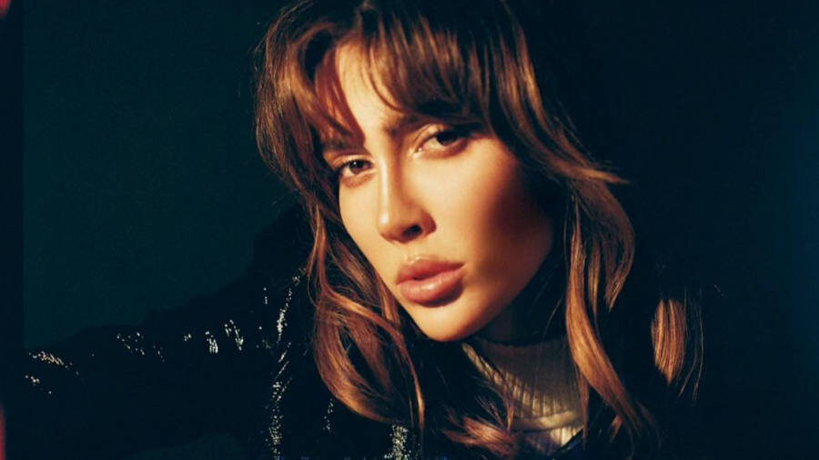 Teddy Quinlivan in a moody, low-light portrait, wearing a black and white varsity-style jacket with tousled hair and intense gaze.