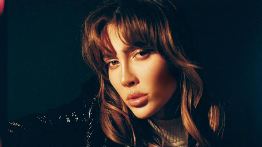 Teddy Quinlivan en un retrato con poca luz, con chaqueta estilo varsity en blanco y negro, cabello despeinado y mirada intensa.