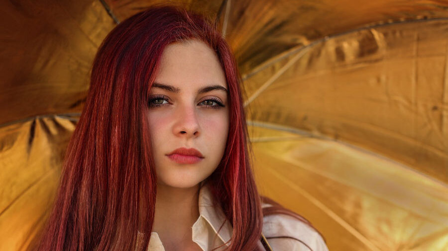 Young woman with long red hair standing in front of a golden background