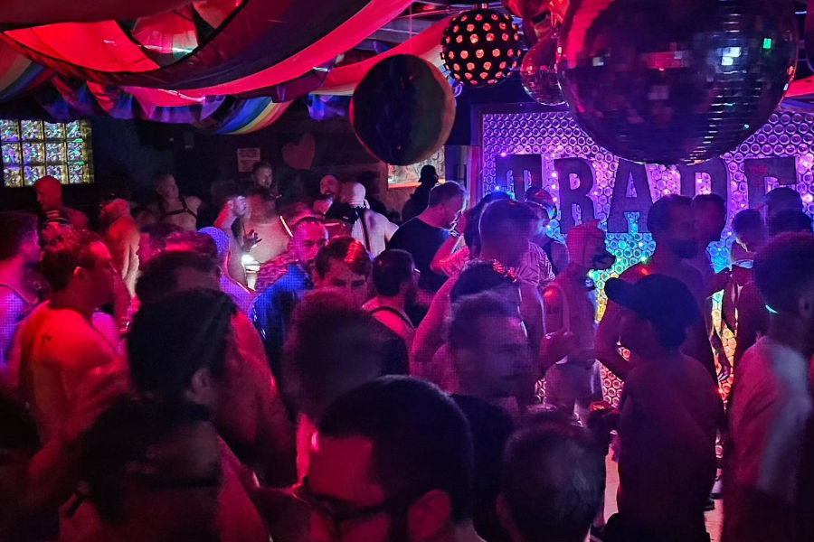 Inside Trade Denver with queer patrons dancing under red lights and rainbow drapery.