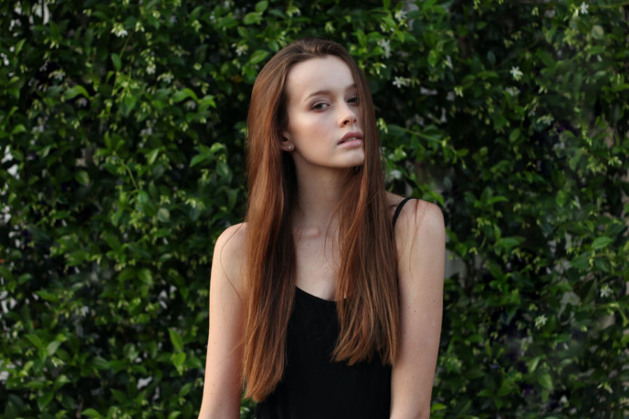 Portrait of an Australian trans woman wearing a black top, posing near leafy plants.