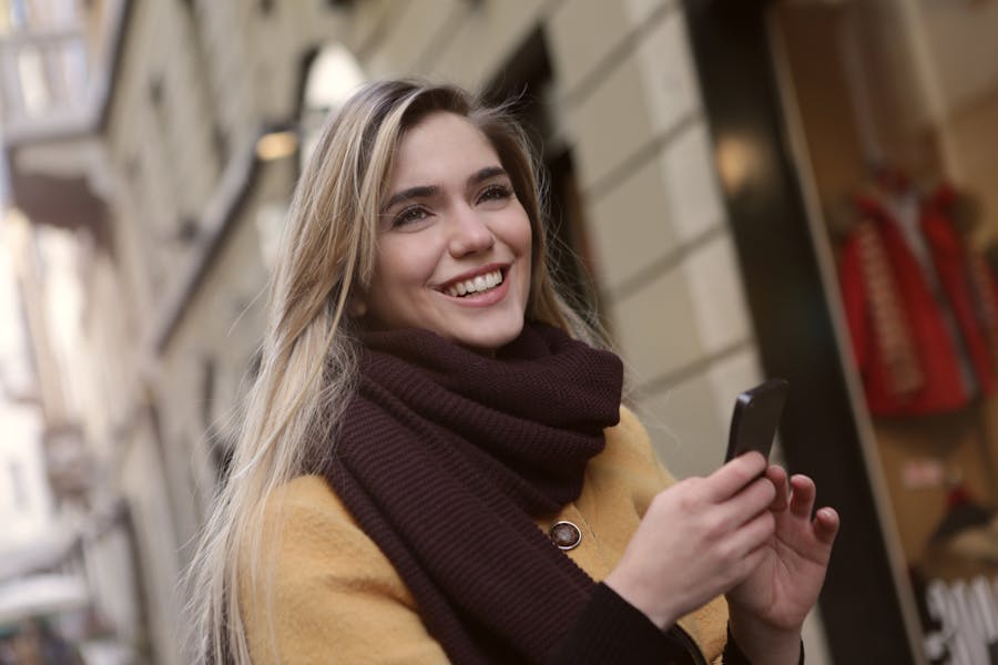 A blonde trans woman smiling and holding her phone on a street in Oklahoma City.