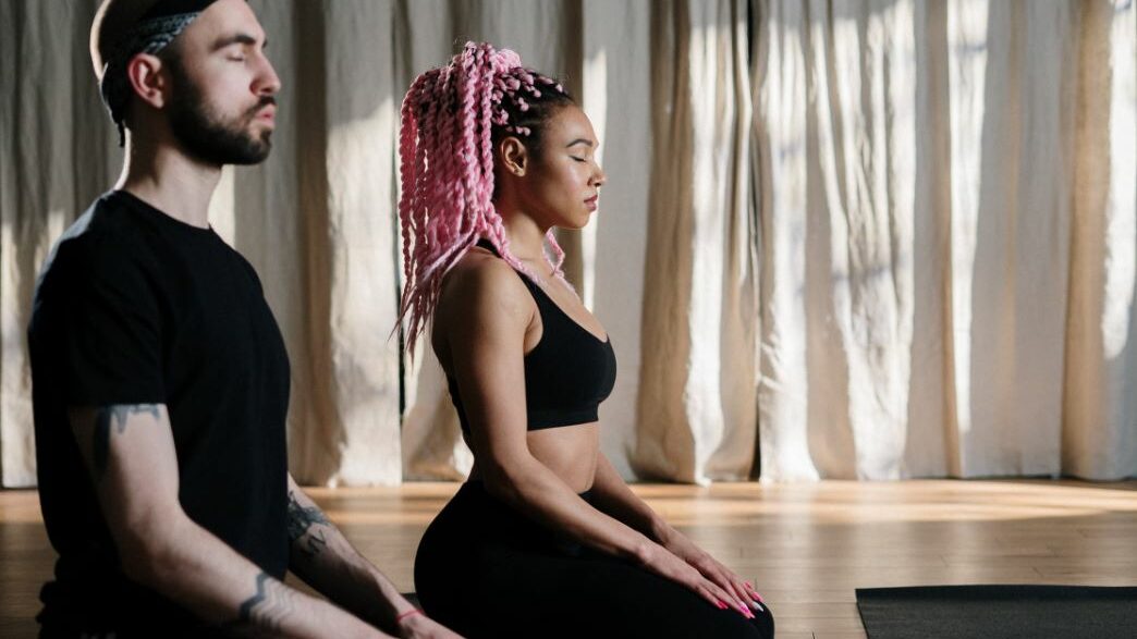 Woman with pink braids and man with headband meditating side by side.