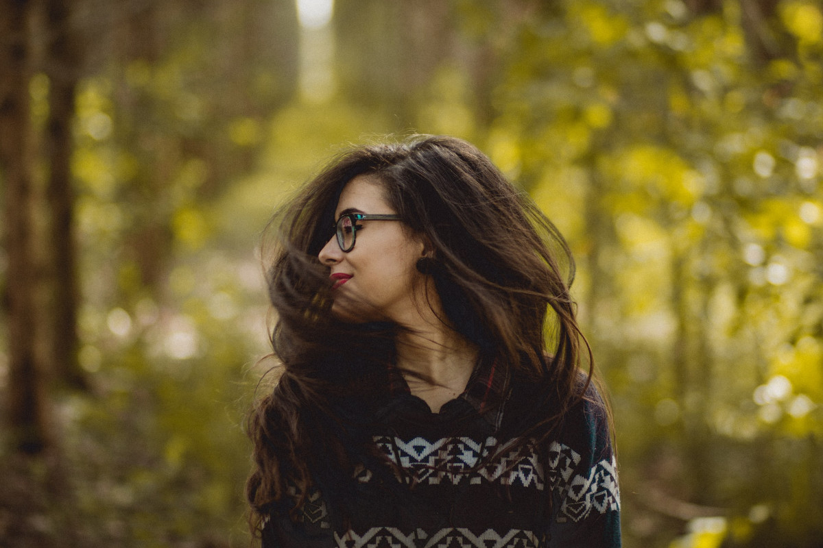 Portrait of a transgender woman from Colombia with long hair and glasses, turning her head in a forest with sunlight.