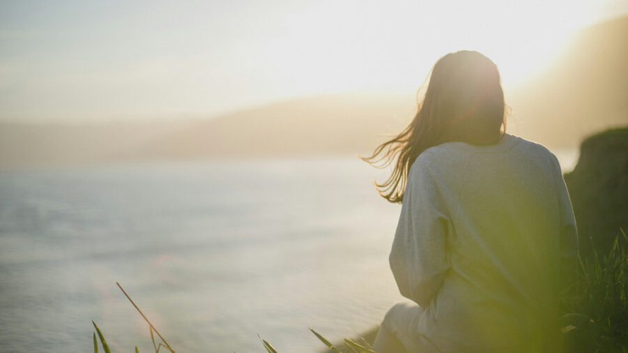 Person sitting on a grassy hill overlooking the water at sunset.