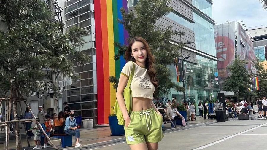 Yoshi Rinrada posing on a Bangkok street in June 2023, with a rainbow flag mural behind her for Pride.